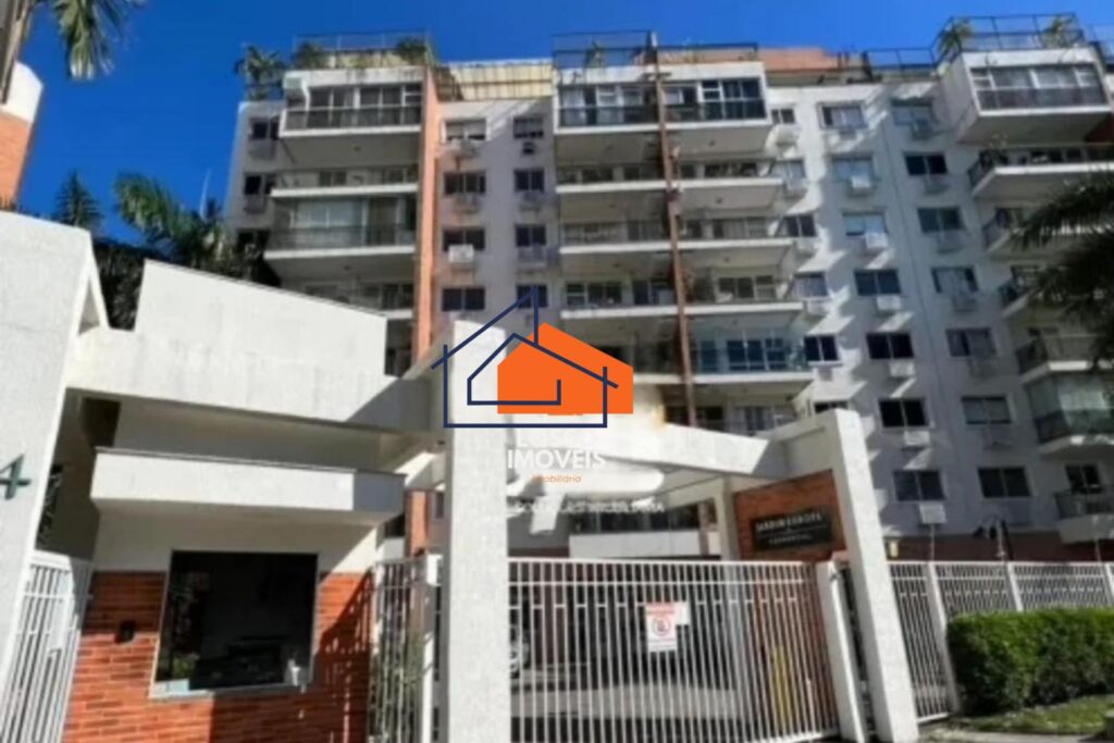 Prédio residencial de vários andares com sacadas, portaria com grades, em área urbana e céu azul.