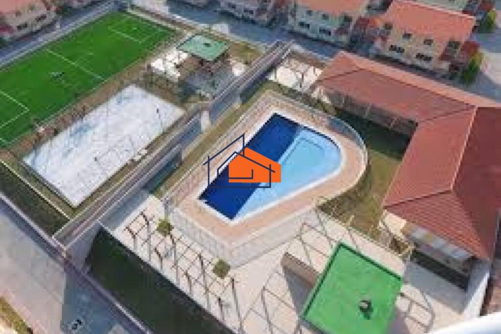 Área de lazer residencial com piscina, quadra esportiva, caminhos pavimentados e telhados vermelhos.