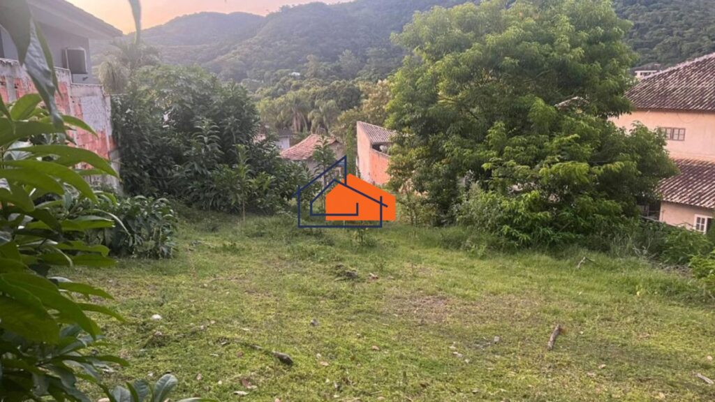 Terreno gramado com árvores e casas ao fundo, encosta de montanha distante.