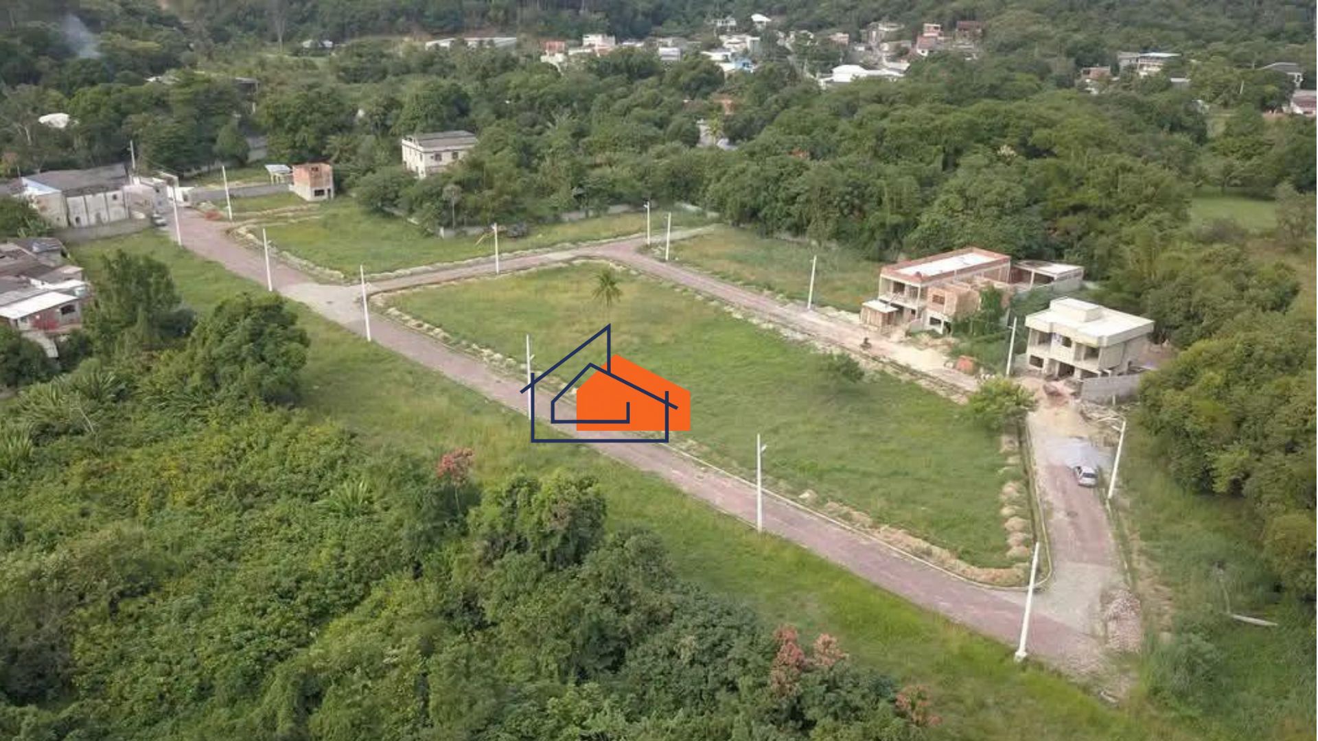 Terreno com áreas verdes, ruas pavimentadas e casas em construção cercado por vegetação densa.